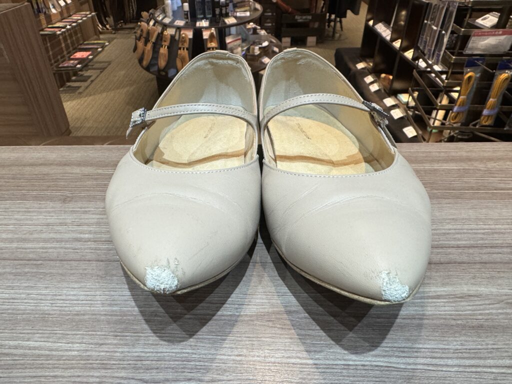 つま先の塗膜が剥がれ下地が見えているポインテッドトーのパンプスを正面から写した補修前の状態