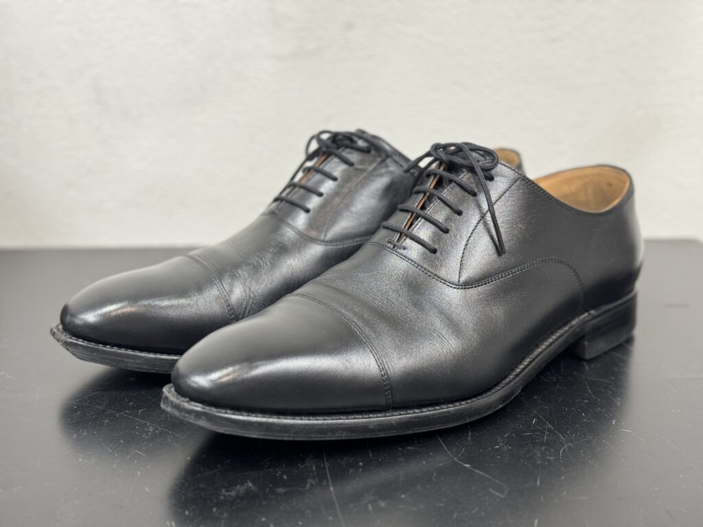 黒のストレートチップ・スコッチグレインの修理前の状態を正面寄りから写した写真。アッパーは比較的きれいだが、ソールに使用感が見られる。