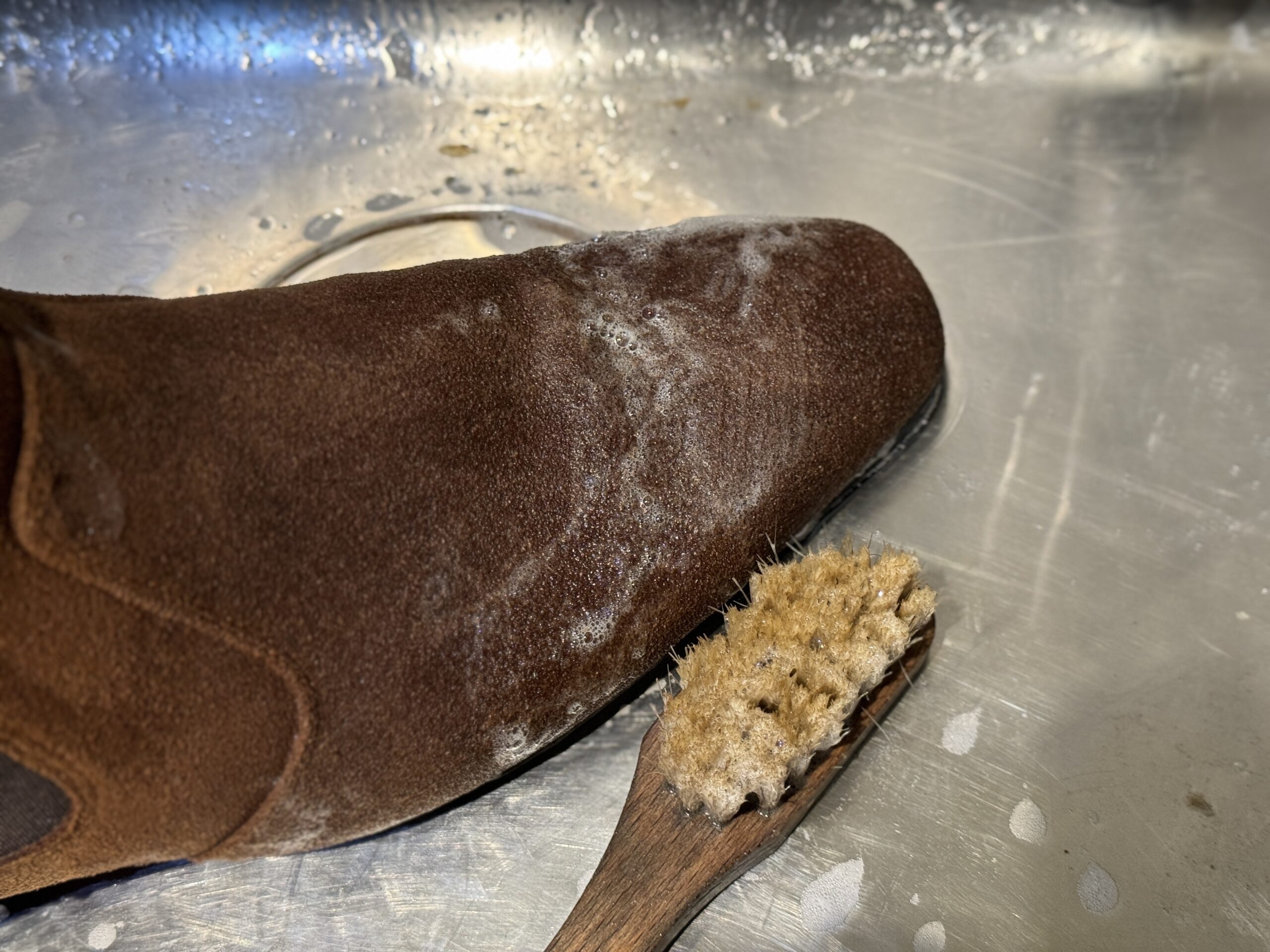 ベージュスエードブーツのクリーニング作業。泡立てながら毛並みを整える工程の一場面。