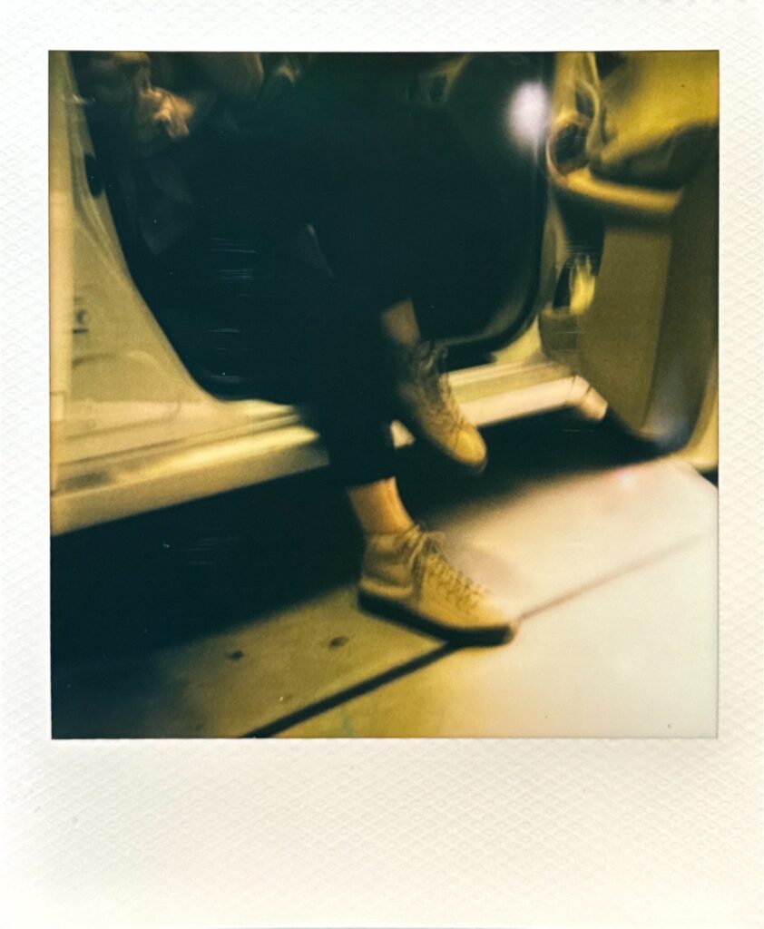 車のドアに腰掛けた人物が、修理後のビルケンシュトックスニーカーを履いているポラロイド写真。夜間の街灯に照らされたシーン。