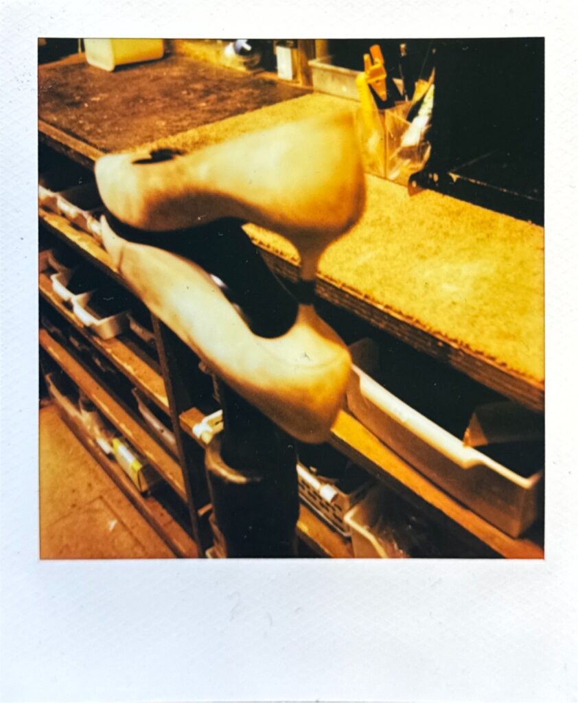 金台に掛けた靴にもう一方を重ねたポラロイド。作業場の空気感を切り取った一枚。