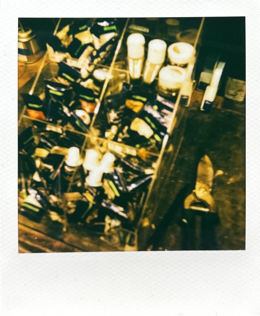 作業台に並ぶ革用の着色塗料チューブと道具を写したポラロイド写真。アトリエの空気感をそのまま切り取った一枚