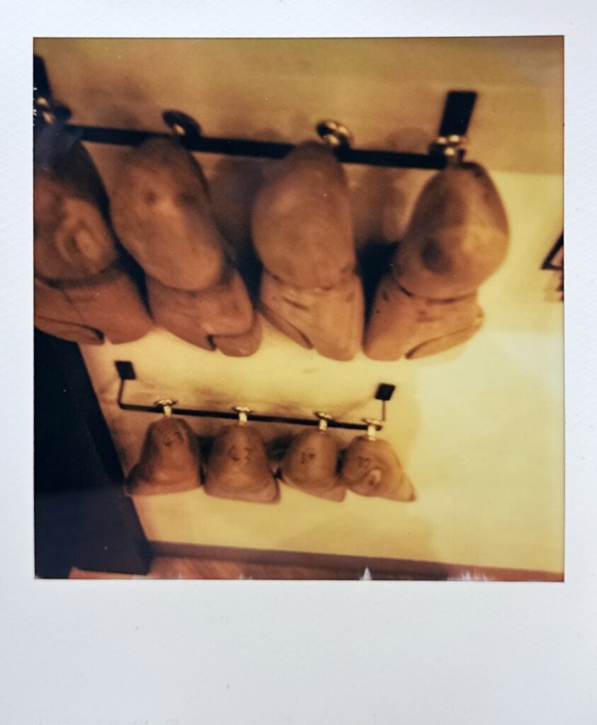 壁に掛けられたシューツリーをポラロイドで撮影した一枚。落ち着いた雰囲気の中で靴の余韻を感じさせるカット