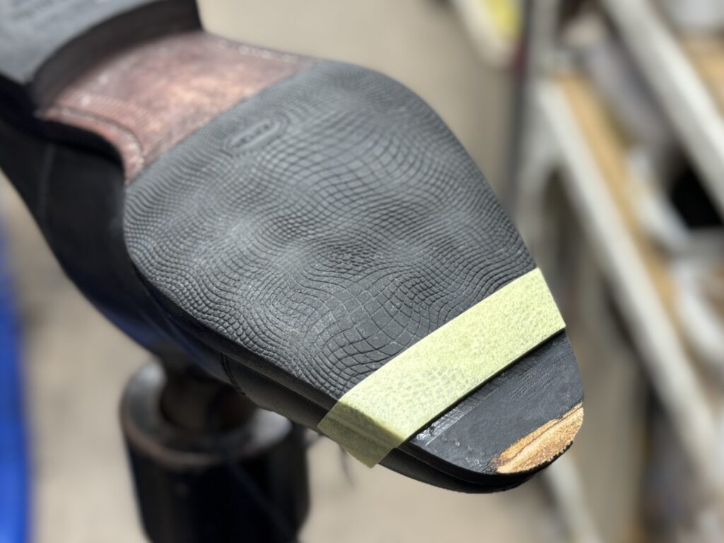 継ぎ足した革端材を研磨し、元のソールと段差が出ないようフラットに整えている途中の写真。マスキングでラインを保持している様子