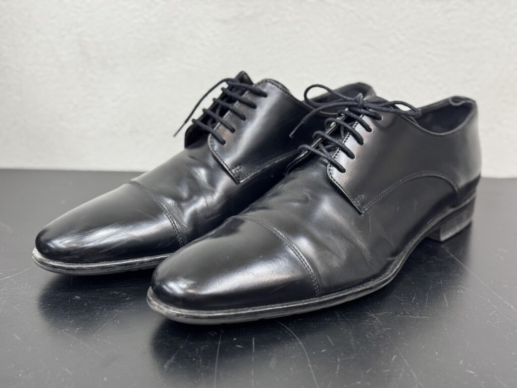 黒のストレートチップが斜め前から写され、履き皺とソールの摩耗が確認できる修理前の状態。