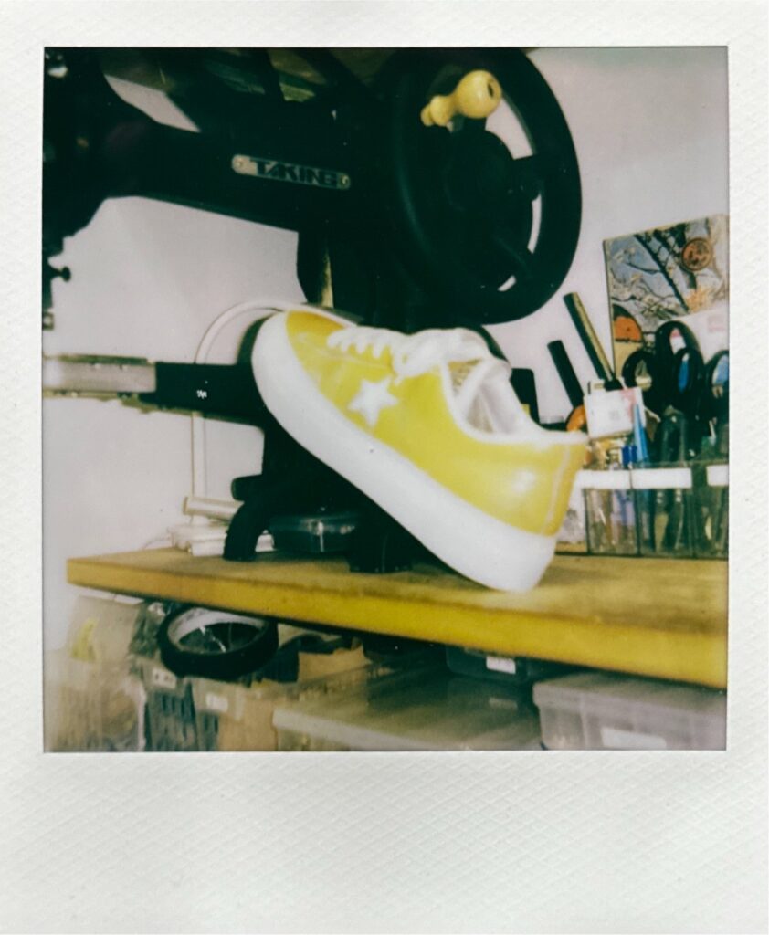 作業場のミシンの上に置かれた、オールソール後のCONVERSE ワンスターを写したポラロイド写真