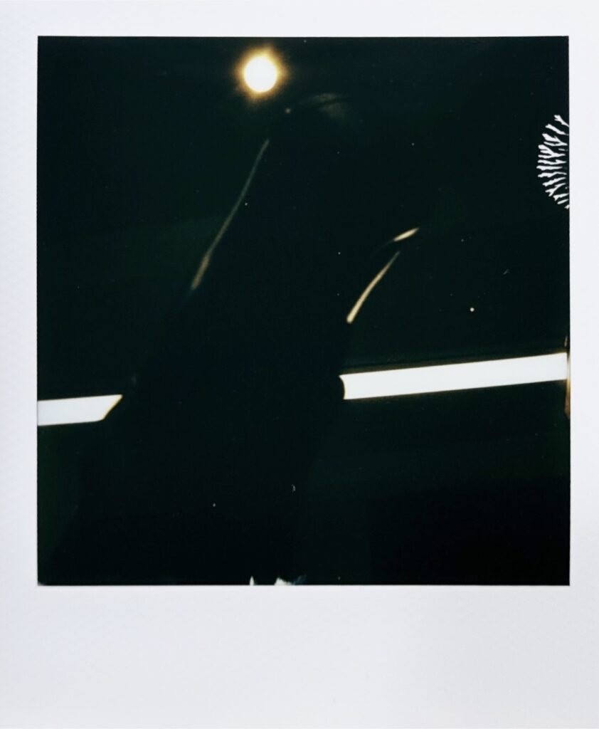 天井方向へ靴を掲げて撮影した抽象的なポラロイド。光源とシルエットだけが浮かび上がる象徴的な一枚。