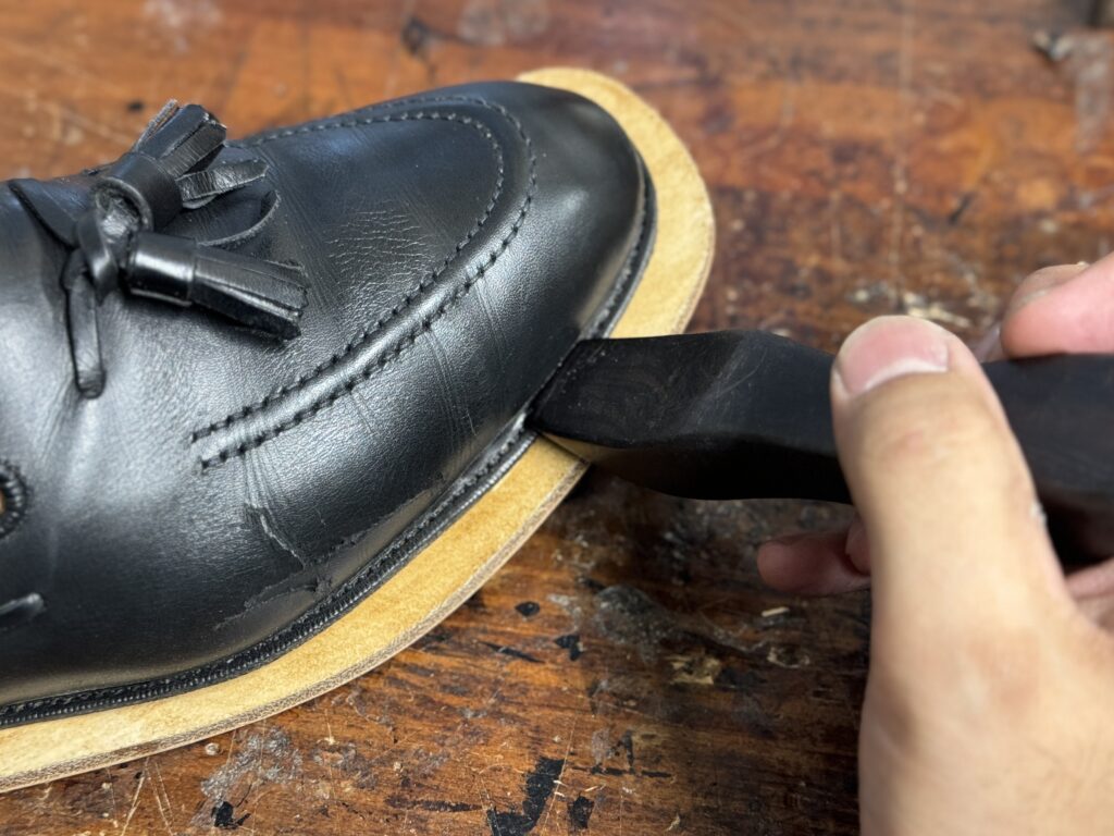 接着段階で、反り返ったウェルトをアウトソール側へ丁寧に沿わせている作業シーン。