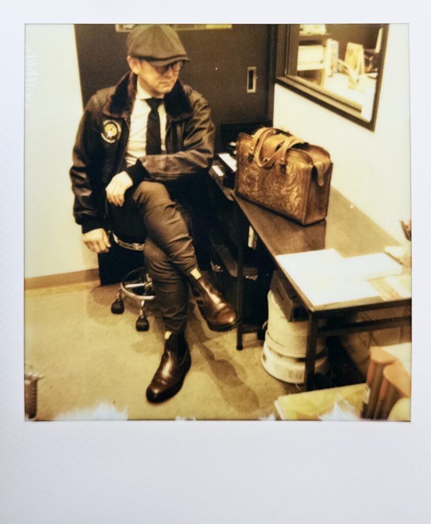 トリッカーズのチェルシーブーツを着用するオーナー様のポラロイド写真（修理後の一足が生活に自然に溶け込む姿）